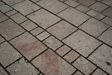 aged stone pavement with irregular square tiles, natural cracks, and warm beige tones. The textured surface shows weathered details and subtle color variations, creating an authentic urban and archite
