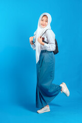 Asian Muslim teenage girl student smiling confidently while carrying backpack and holding pencil, ready to study and learn, education and back to school concept.