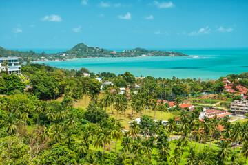 Aerial view of tropical coastal landscape with lush palm trees, hillside villas and turquoise sea under a bright sunny sky on Koh Samui island, Thailand. Summer vacation destination in Asia
