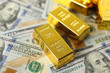 Shiny gold bars and dollar banknotes on table, closeup