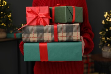 Woman with gift boxes in room decorated for Christmas, closeup. Bokeh effect