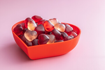 Heart shaped jelly candies in bowl on pink background.