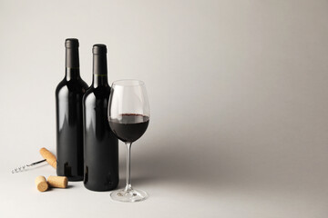 Tasty red wine in glass, bottles, corks and corkscrew on light grey background, space for text