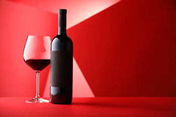 Bottle and glass of tasty wine on red background. Space for text