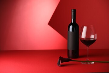 Tasty wine in bottle, glass and flower on red background. Space for text
