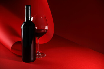 Bottle and glass of tasty wine on red background. Space for text