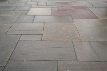 Modern stone pavement texture with square tiles in neutral gray and beige tones. Urban sidewalk background for architecture, design, and construction projects. Clean geometric pattern of paving slabs.