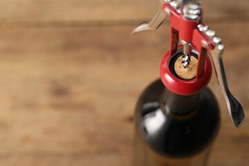 Bottle of luxury wine with corkscrew on table, closeup. Space for text