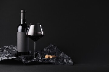Bottle of wine, wineglass and paper on black background, space for text