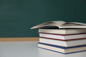 Stack of books on desk against chalkboard. Space for text