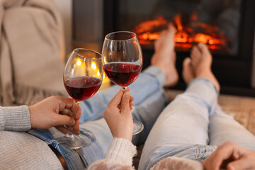 Couple with glasses of wine near fireplace on floor at home, selective focus