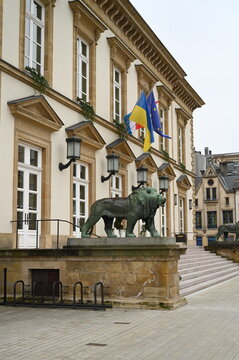 Historic European building with large windows, ornate architectural details, and a bronze animal sculpture placed on the entrance terrace. Colorful flags hang above the doorway, creating a classic civ