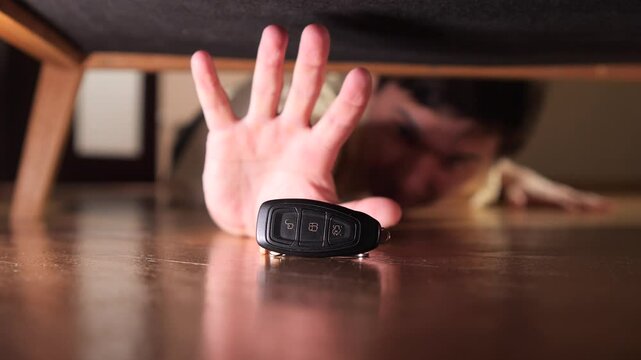 Man reaching for car keys underneath furniture