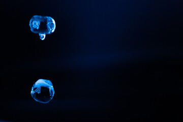 Two translucent blue liquid droplets suspended in a dark, minimal environment, glowing softly with reflections and creating a futuristic, ethereal mood. Includes copy space.
