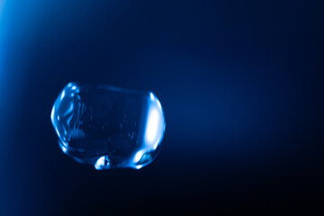 A glowing, translucent blue bubble floats against a dark blue background, with reflections and light streaks creating a futuristic and surreal effect. Includes copy space.