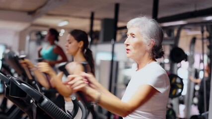Elderly athletic woman in sportswear training on elliptical machine in gym - Powered by Adobe