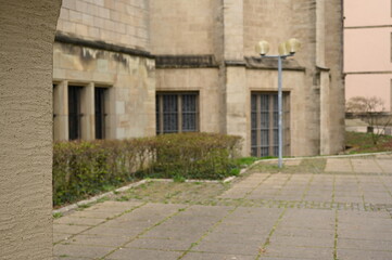 Historic stone building exterior with arched passages, textured sandstone walls, and trimmed bushes in a quiet courtyard. Classic architectural details suitable for heritage, university, and European