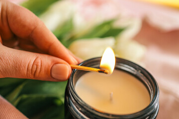 Close-up of a hand lighting a candle with a match. Soft focus on white tulips and a pink jacket in...