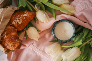 Cozy still life with a burnt candle in an amber glass jar surrounded by white tulips, a pink denim...