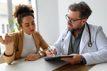 Male healthcare worker with clipboard consulting and explaining diagnostic results to patient in...