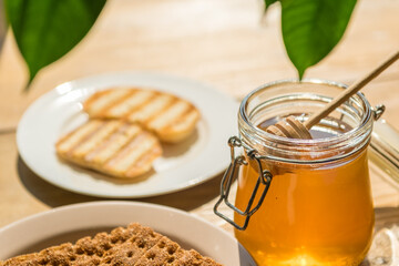 Honey Jar With a Wooden Stick Beside Crunchy Cookies on a Plate in a Bright Kitchen perfect for...