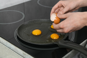 Woman breaking egg into frying pan in kitchen, closeup