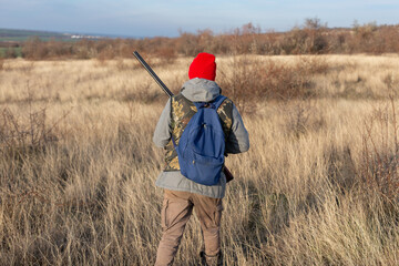 Mature hunter man holding a shotgun and walking through a field