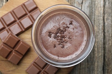 Tasty chocolate milk with shavings and pieces on wooden table, top view