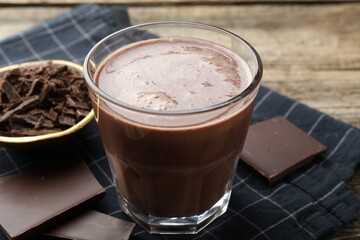 Tasty chocolate milk with shavings and pieces on wooden table, closeup