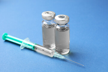 Hepatitis vaccine in glass vials and syringe on blue background, closeup