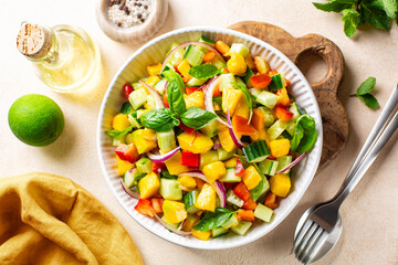 Bright mango salad made with red bell pepper, cucumber, red onion, fresh mint, basil and lime, olive oil and honey dressing. Top view.