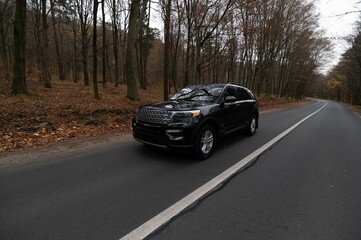 Fototapeta premium A black SUV cruising along a picturesque road surrounded by autumn foliage in a serene forest setting.