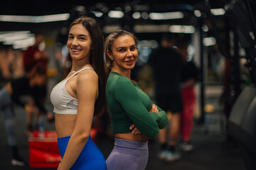 Fototapeta premium Two fit women posing back to back in gym after workout