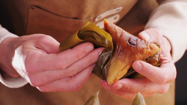 Hand holding zongzi (rice dumpling) with savoury fillings wrapped in bamboo or reed leaves.