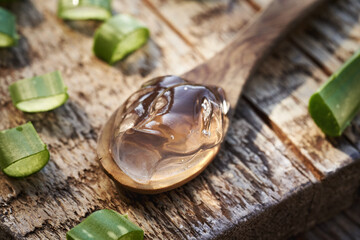Clear aloe vera gel on a wooden spoon with fresh sliced aloe vera leaves