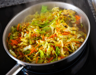 Chopped cabbage braising with vegetables in open pan. Preparing food.