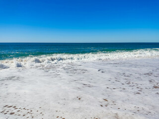Serene ocean view with foamy waves under a clear, vibrant blue sky. Evokes tranquility, summer vibes. Ideal for travel, vacation, or relaxation themes.