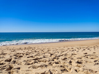 Serene beach scene with footprints in the sand, calm blue ocean, and clear sky. Perfect for travel, vacation, or summer concepts. Evokes peace and relaxation.