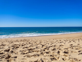 Serene beach scene with footprints in the sand, meeting a calm, turquoise ocean under a clear blue sky. Perfect for travel, vacation, or summer themes.
