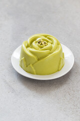 Vegan Pistachio cream dessert in the shape of a rose. On a plate. Light background. Close-up