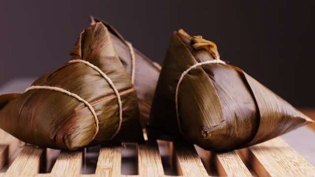 Hand holding zongzi (rice dumpling) with savoury fillings wrapped in bamboo or reed leaves.
