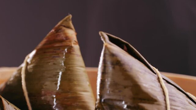 Hand holding zongzi (rice dumpling) with savoury fillings wrapped in bamboo or reed leaves.