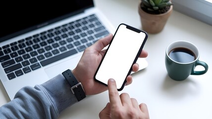 Mockup of Hand Holding Smartphone with Blank Screen at Desk with Laptop and coffee