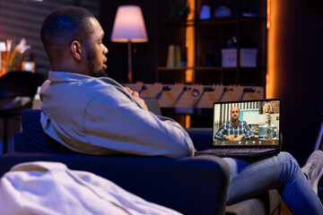 Male remote worker waving at his associates during virtual meeting, showcasing effectiveness of online tools and internet connection. Young adult sharing insight in a briefing session.