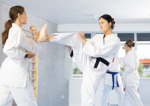 Experienced Asian female karateka in kimono and black belt honing kicking techniques during kumite at training session