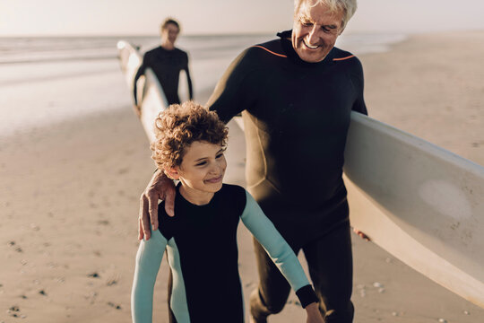 Multigenerational family of male surfers getting ready to surf on a sandy beach