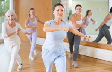 Obraz premium Group of happy young mature sports women in activewear exercising dynamic dancing movemens in modern gym studio