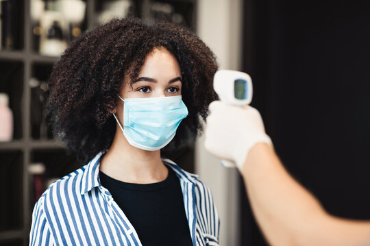Young black woman in protective mask getting temperature check up in salon, close up