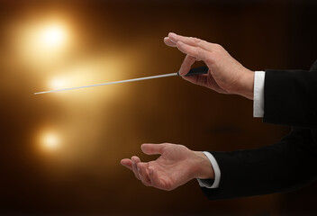 Conductor directing orchestra with baton in concert hall, closeup