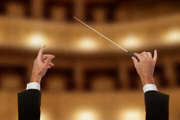 Conductor directing orchestra with baton in concert hall, closeup © New Africa